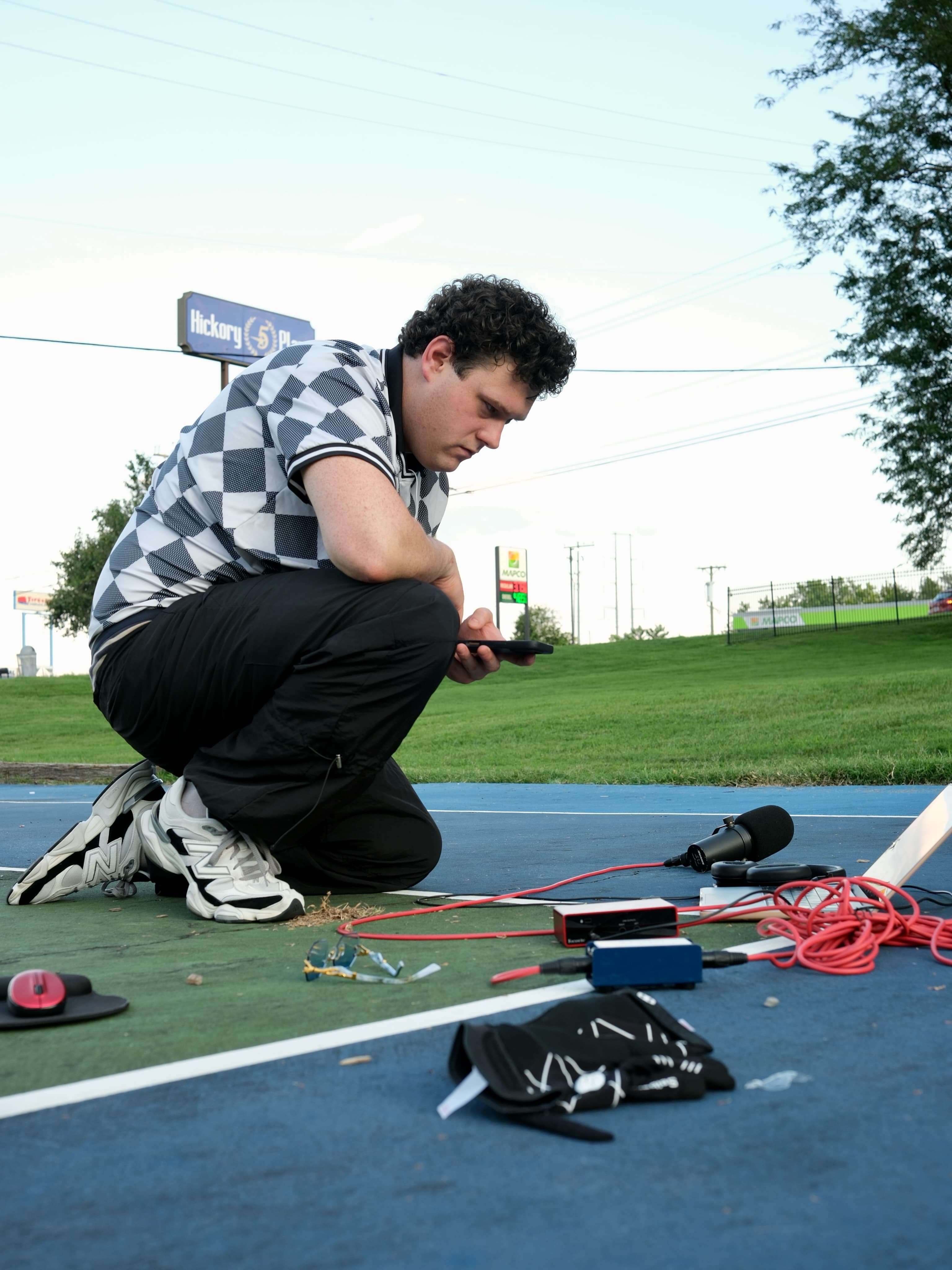 BRAVEN crouching over his phone beside a microphone and recording equipment on the court.
